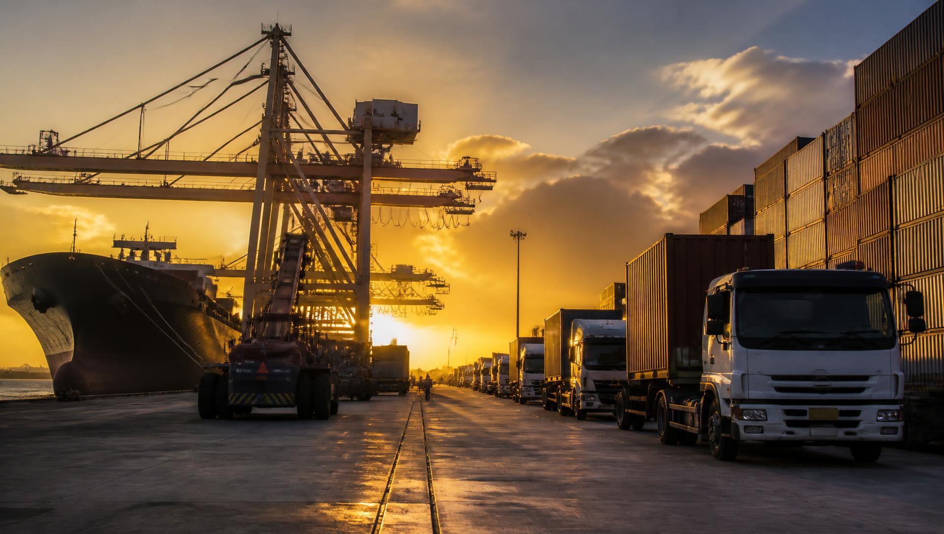 Port terminal with cranes, containers and trucks in operation at sunset
